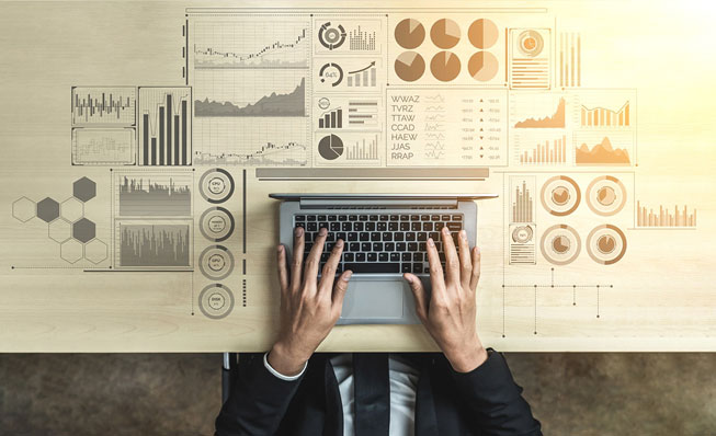 A person sitting at their laptop with figures representing big data spread out on the table around it.