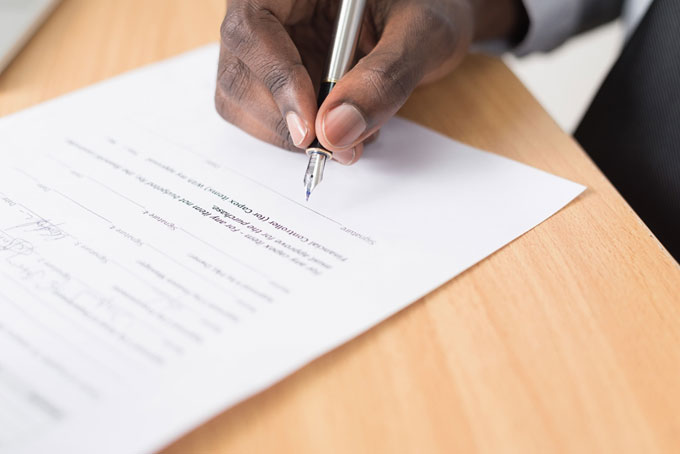 A hand signing a contract on the dotted line with a fountain pen.