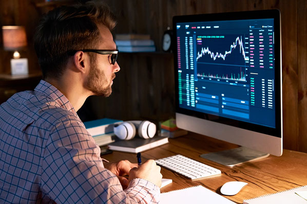 A man sitting at his desk looking at data on a computer screen