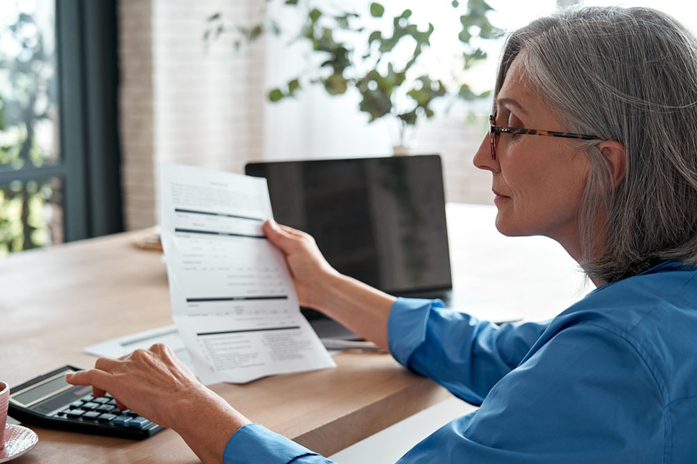 A mature businesswoman holding a paper bill and manually calculating.