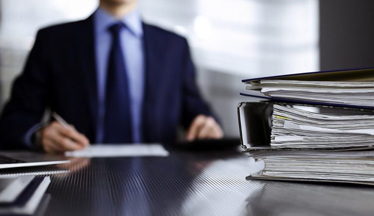 Binders of papers for invoice scanning and data capture with man wearing a blue blazer in background