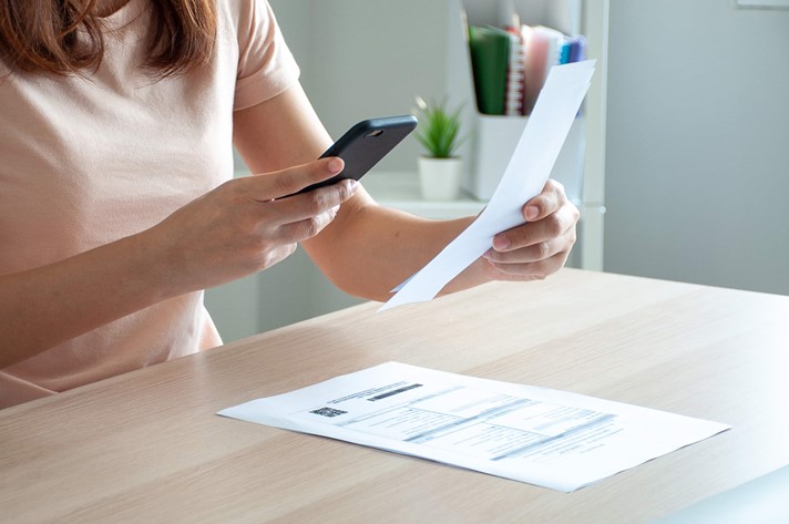 A woman processing invoice payments from home, using invoice capture technology on her smartphone