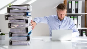 Office worker pushing paper invoices away for greater time efficiency through einvoicing benefits Filename: Einvoicing-benefits-time-efficienc