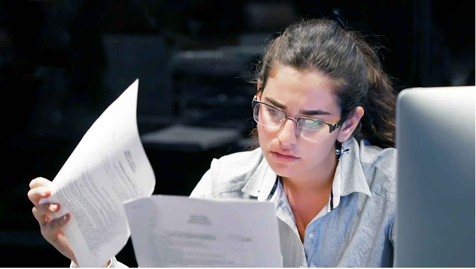 OCR vs AI OCR – woman looking through documents, sitting next to a computer