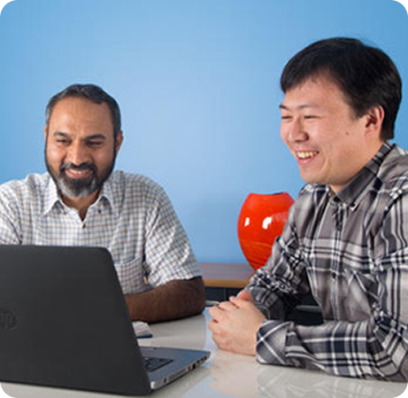 Two men sitting at a table looking at a laptop